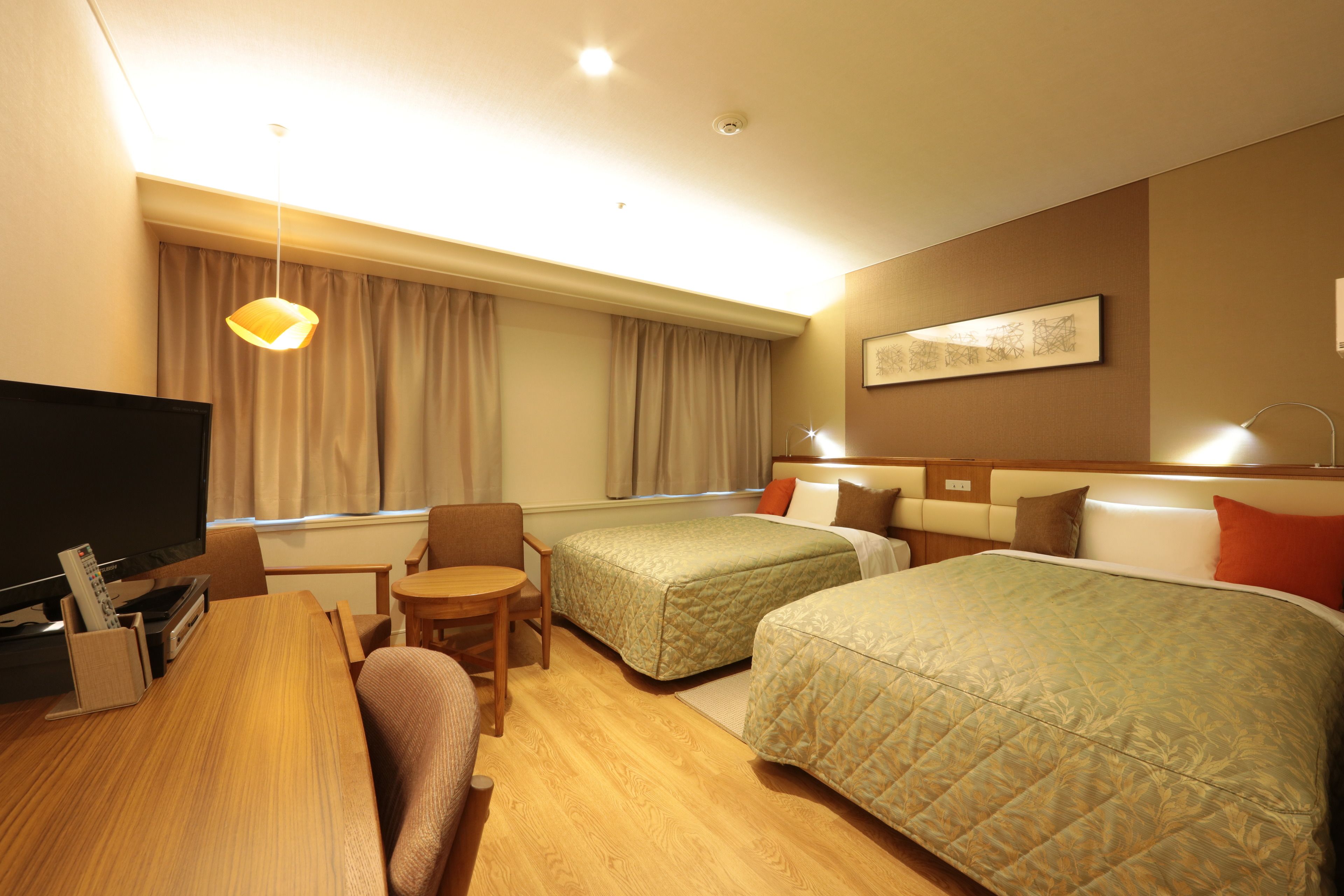A hotel room with two beds, a desk with a TV, a chair, and a window with curtains.