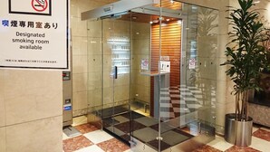 A hotel lobby with a designated smoking room sign, a glass elevator, and a potted plant. - Hotel Monarque Tottori (Tottori)