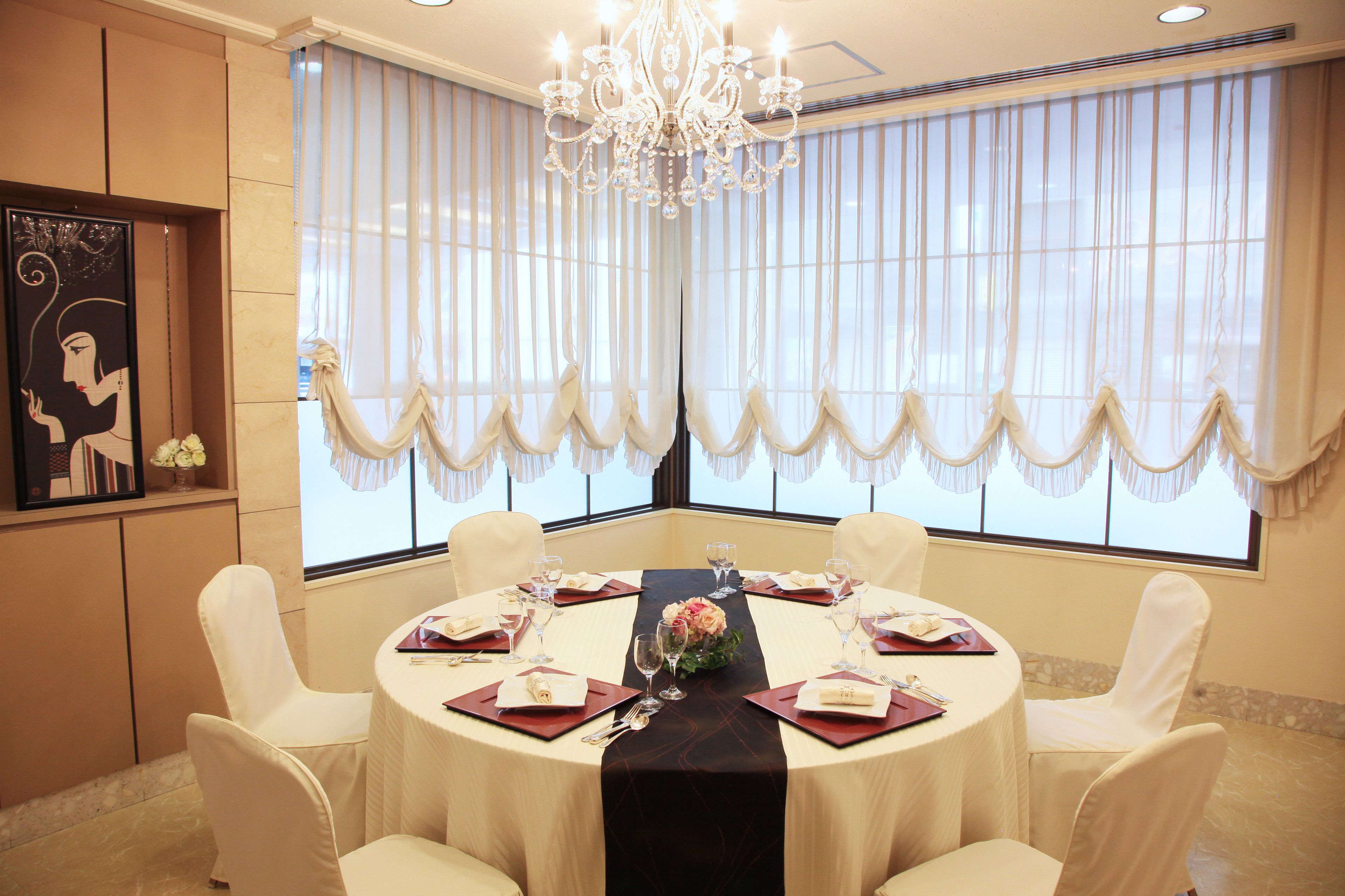 Una mesa de comedor redonda con sillas blancas, una araña y un centro de mesa floral.