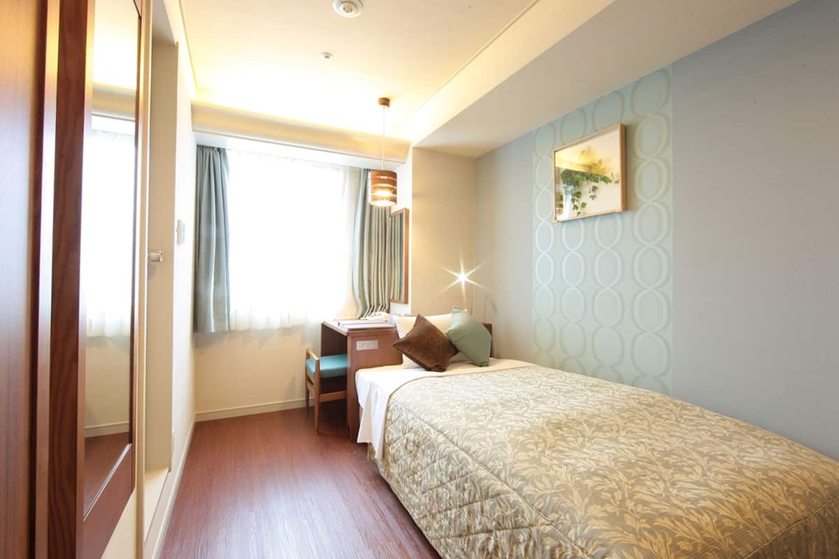 A hotel room with a bed, a desk, a chair, and a window with curtains.