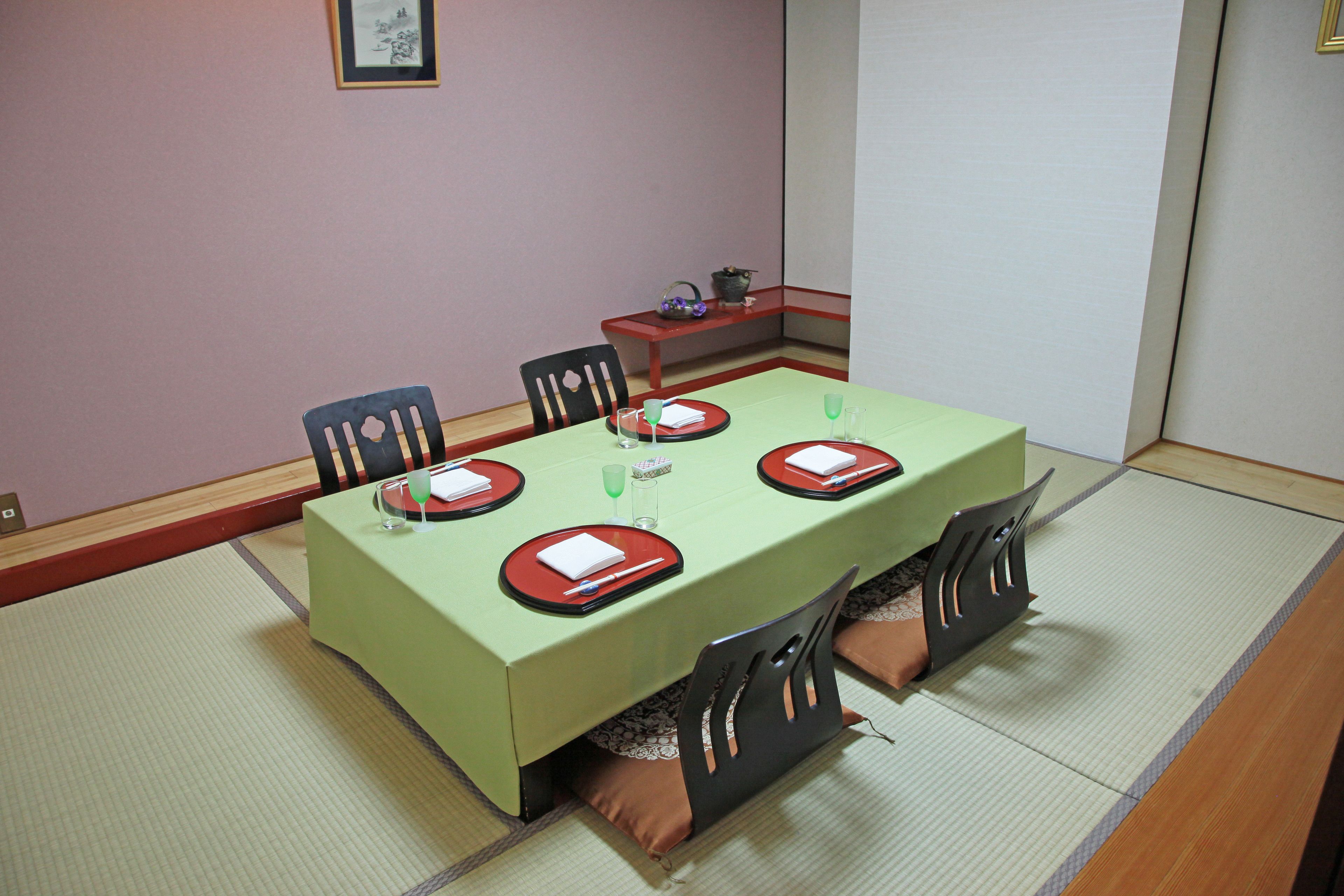 Una mesa de comedor dispuesta con platos, vasos y una jarrón, rodeada de sillas.