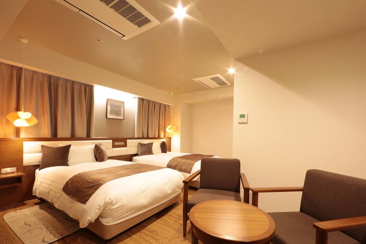 A hotel room with two beds, a wooden floor, a small round table, and two chairs.