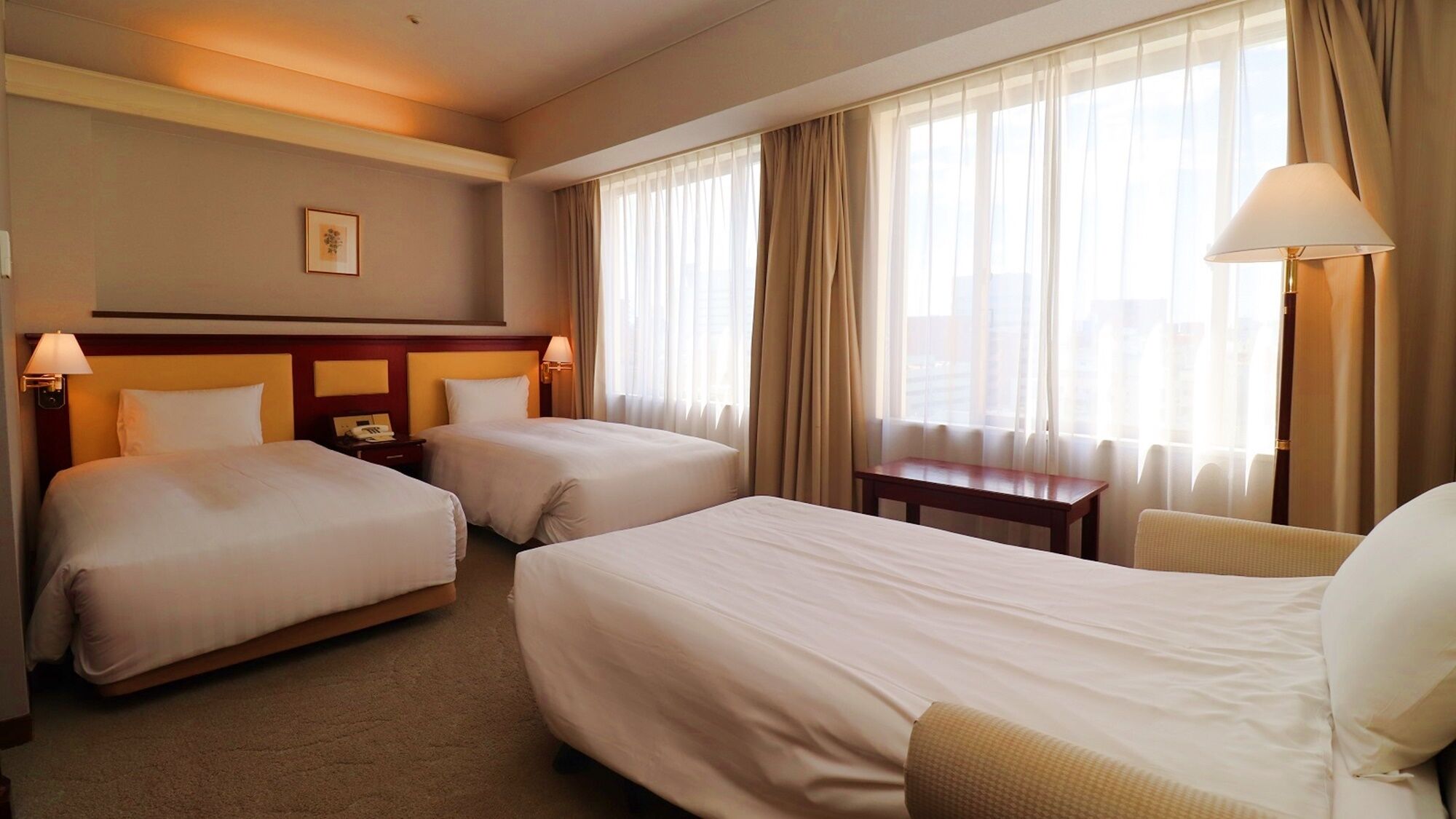A hotel room with two beds, a desk, a chair, a lamp, and a picture on the wall.