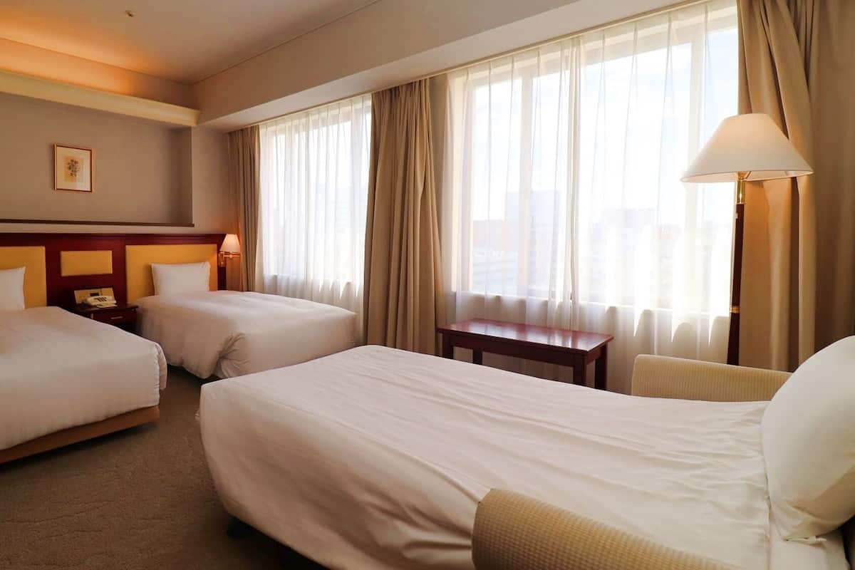 A hotel room with two beds, a desk, a chair, a lamp, and a picture on the wall.