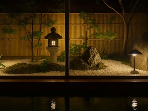 A traditional Japanese garden with a stone lantern, rocks, and a wooden fence at night.