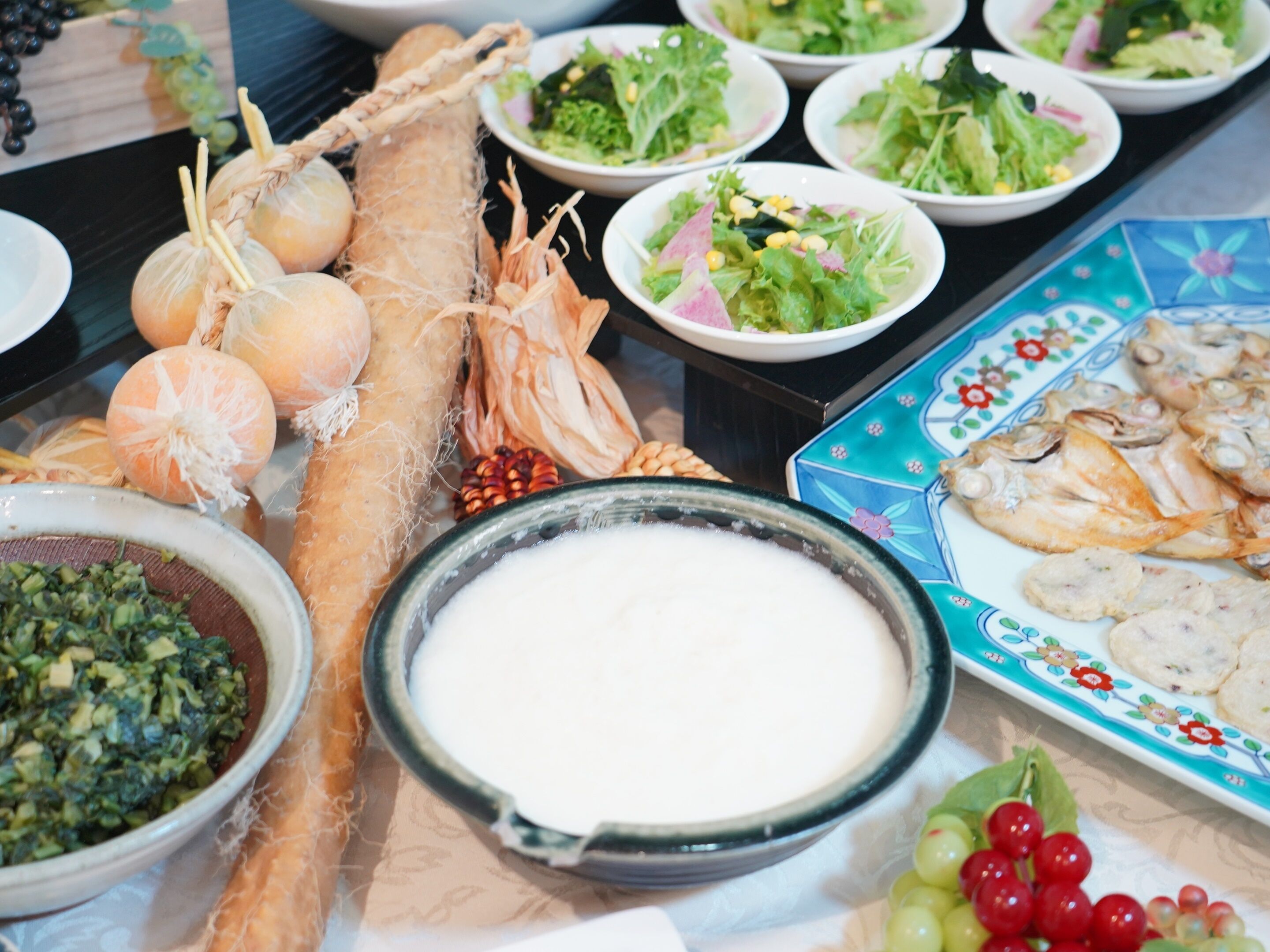 Una mesa con diversos alimentos, entre ellos verduras, pescado y un bol de salsa blanca.