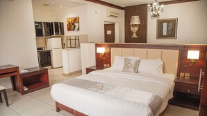 Una habitación de hotel con una cama grande, mesitas de noche, un escritorio y una kitchenette.