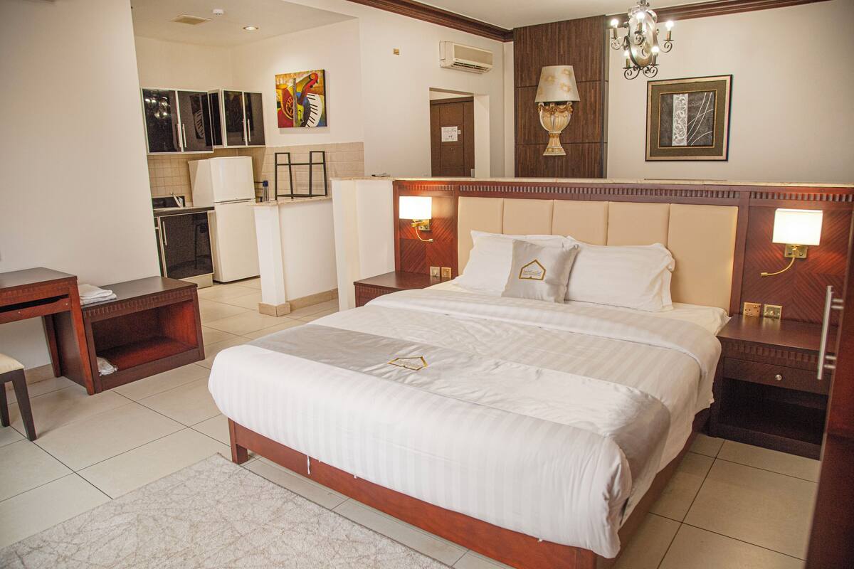 A hotel room with a large bed, bedside tables, a desk, and a kitchenette.