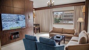 Una sala de estar con televisión, dos sofás, una mesa de centro y una ventana con cortinas.