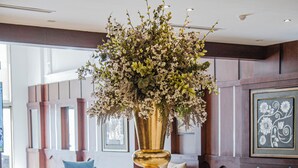 Un moderno hall de entrada con una mesa de centro de vidrio, sofás azules y un gran arreglo floral en un jarrón dorado.