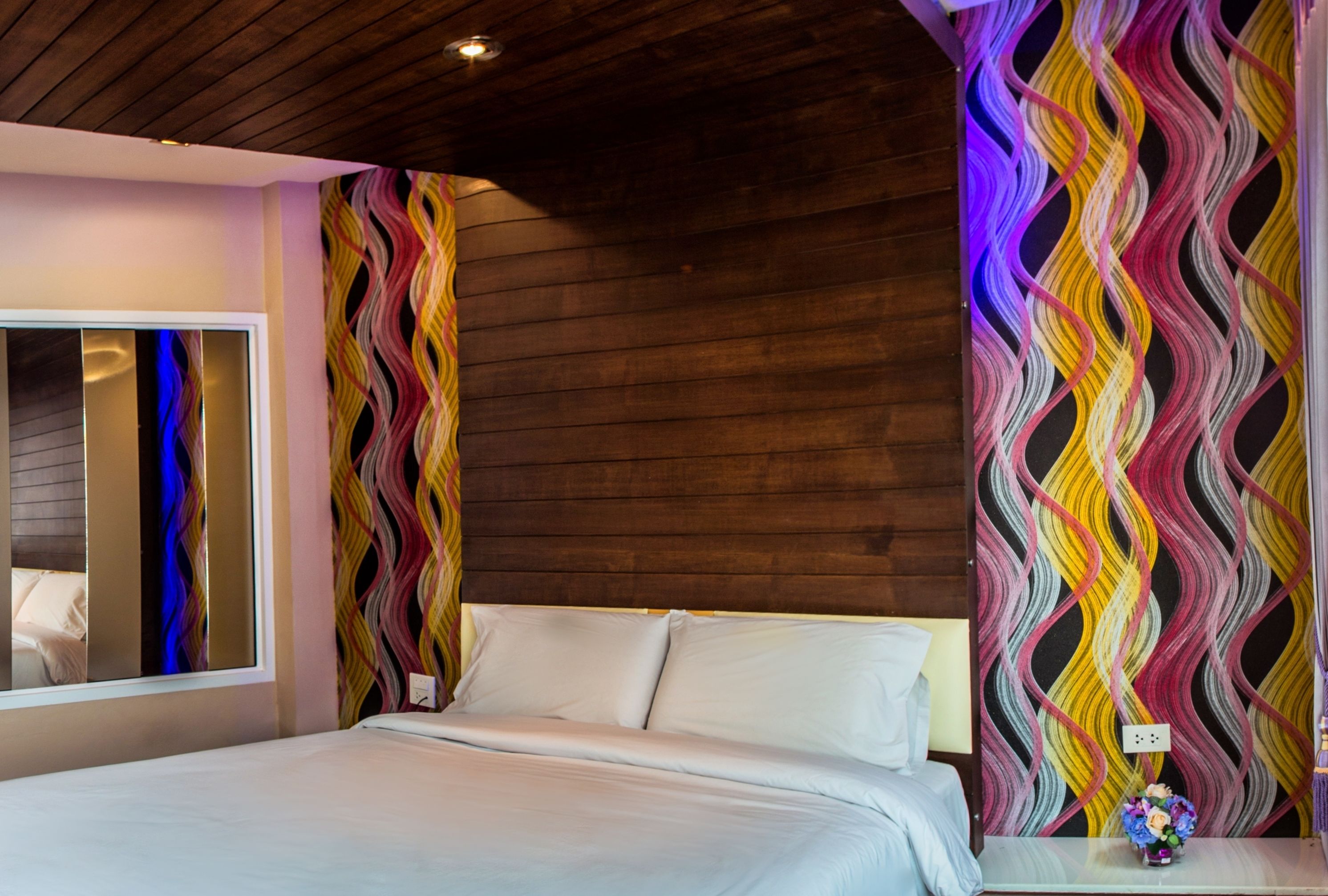 Un dormitorio con cama, espejo y pared con un diseño ondulado y colorido.
