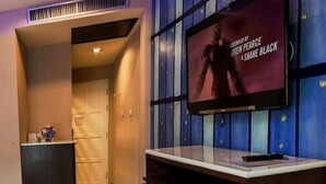 A modern hotel room with a large flat-screen TV mounted on a blue and white wall, a wooden desk, and a door leading to another room. - The Ring Hotel (Hat Yai)