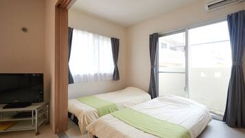 A hotel room with two beds, a TV on a stand, and a balcony with curtains.