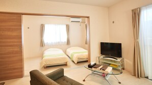 A hotel room with two beds, a TV on a glass table, a sofa, and a sliding door closet. - Rainbow Terrace (Ginowan)