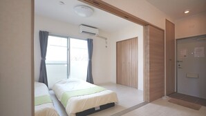 A bedroom with two beds, a wooden wardrobe, and a sliding door. - Rainbow Terrace (Ginowan)