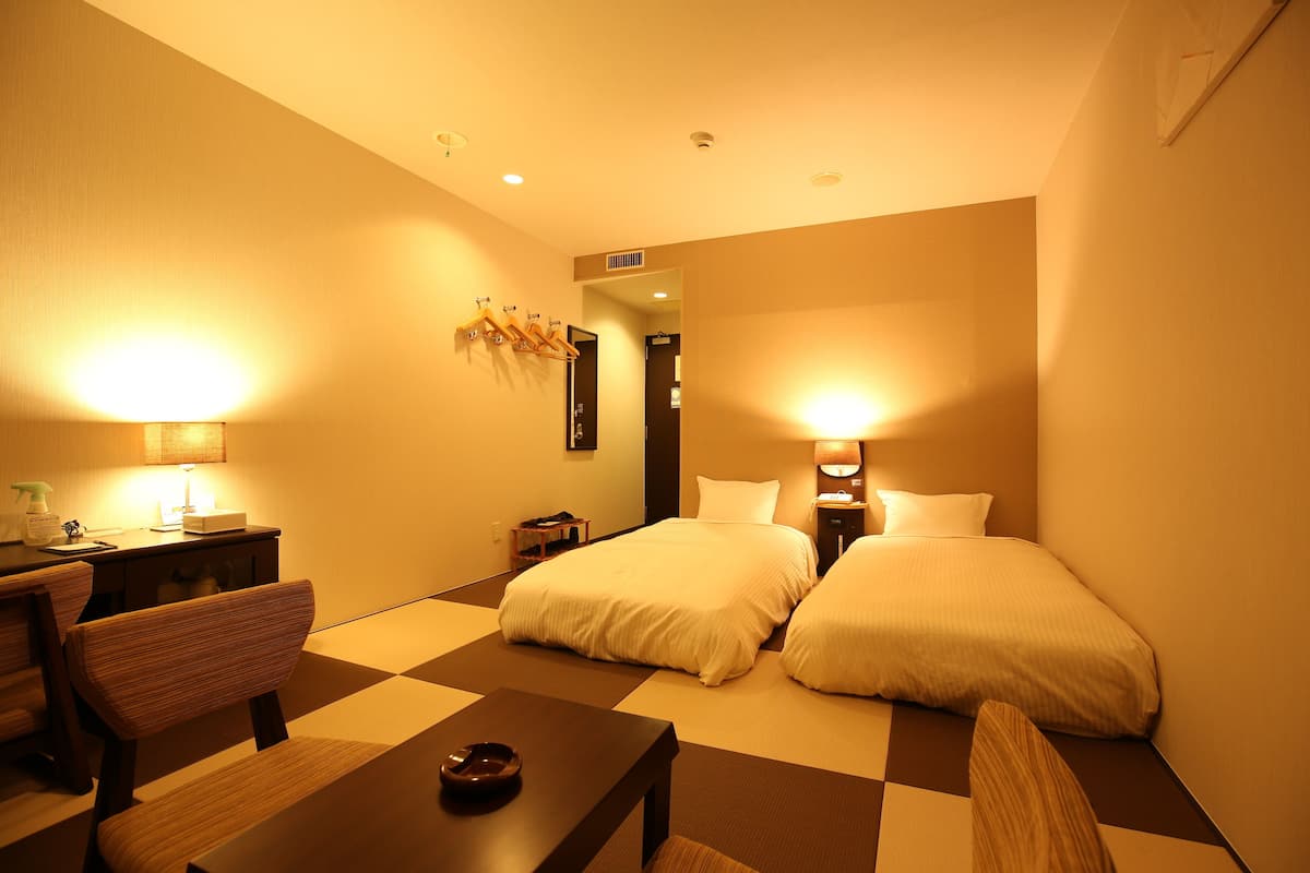 A hotel room with two beds, a desk, a chair, and a table.
