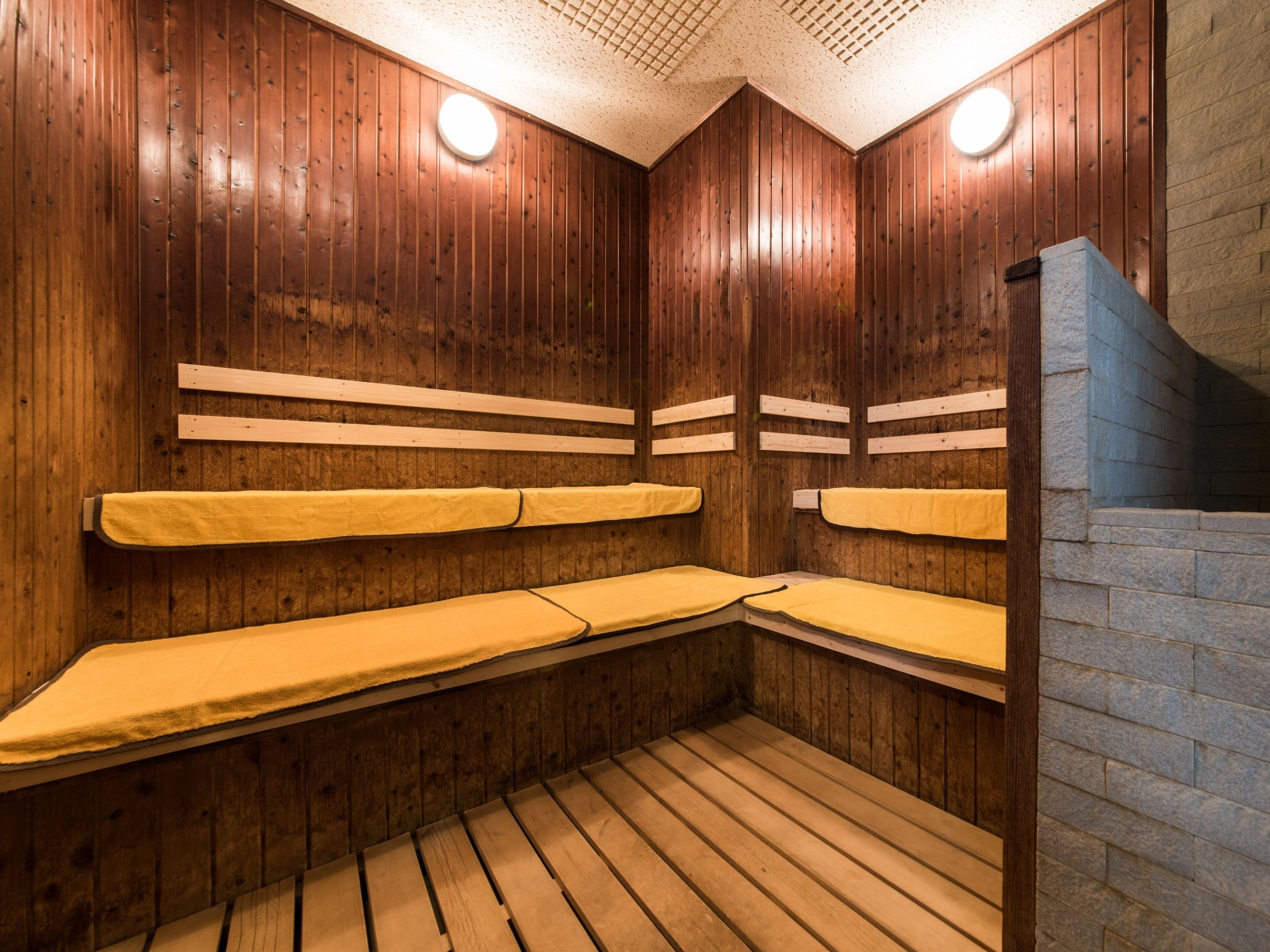 Una sauna con paredes y bancos de madera, una pared de piedra en un lateral y un techo con patrón de cuadrícula.