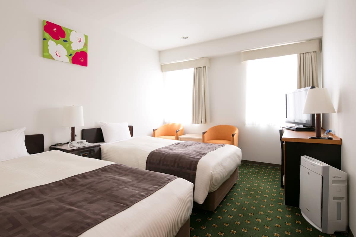 A hotel room with two beds, a desk with a lamp, a television, and a small refrigerator.