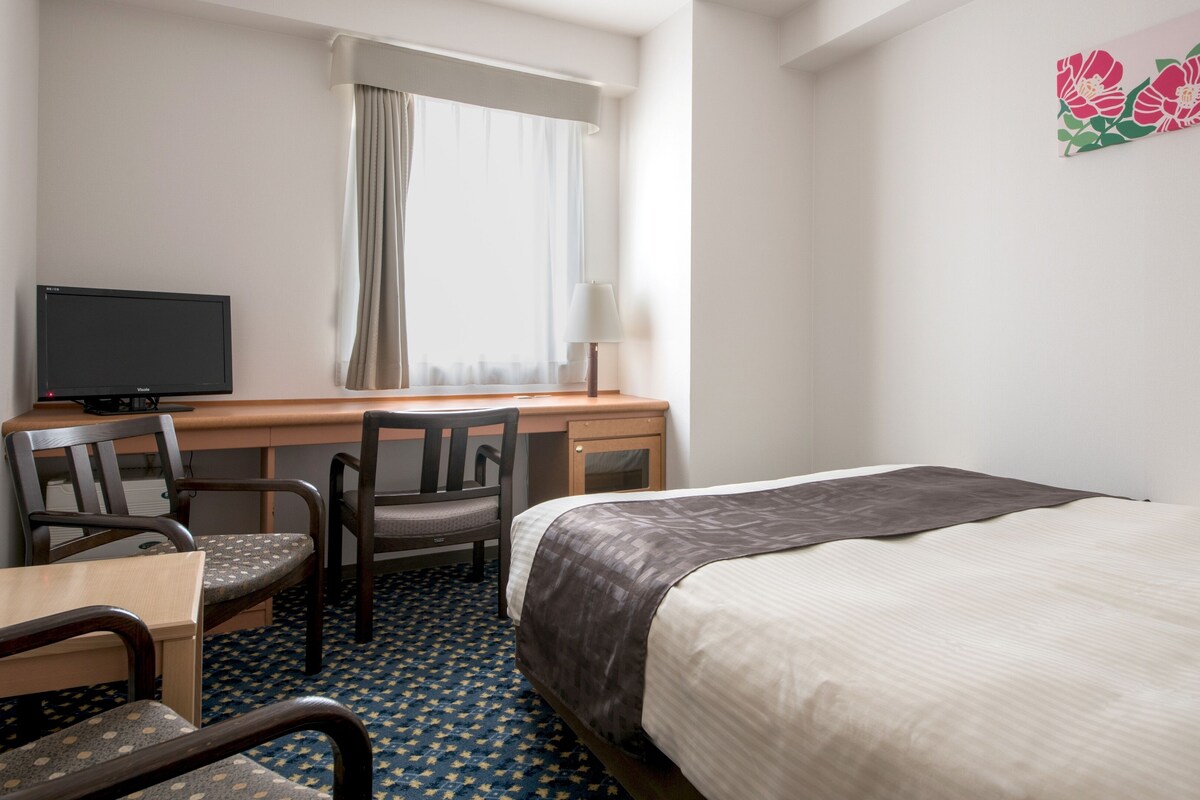 A hotel room with a bed, two chairs, a desk with a computer, and a TV.