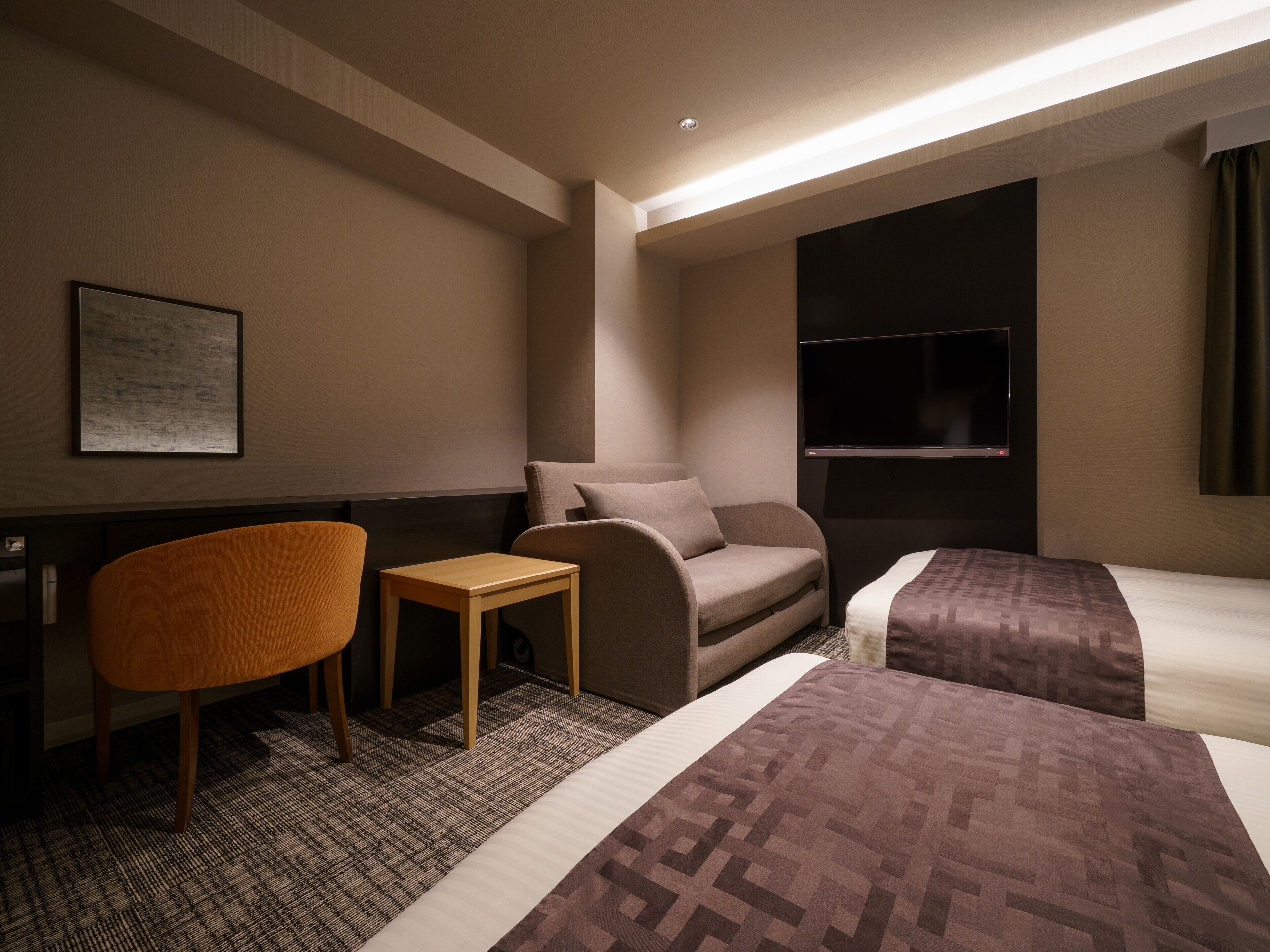 A hotel room with a bed, two armchairs, a small table, a TV, and a framed picture on the wall.