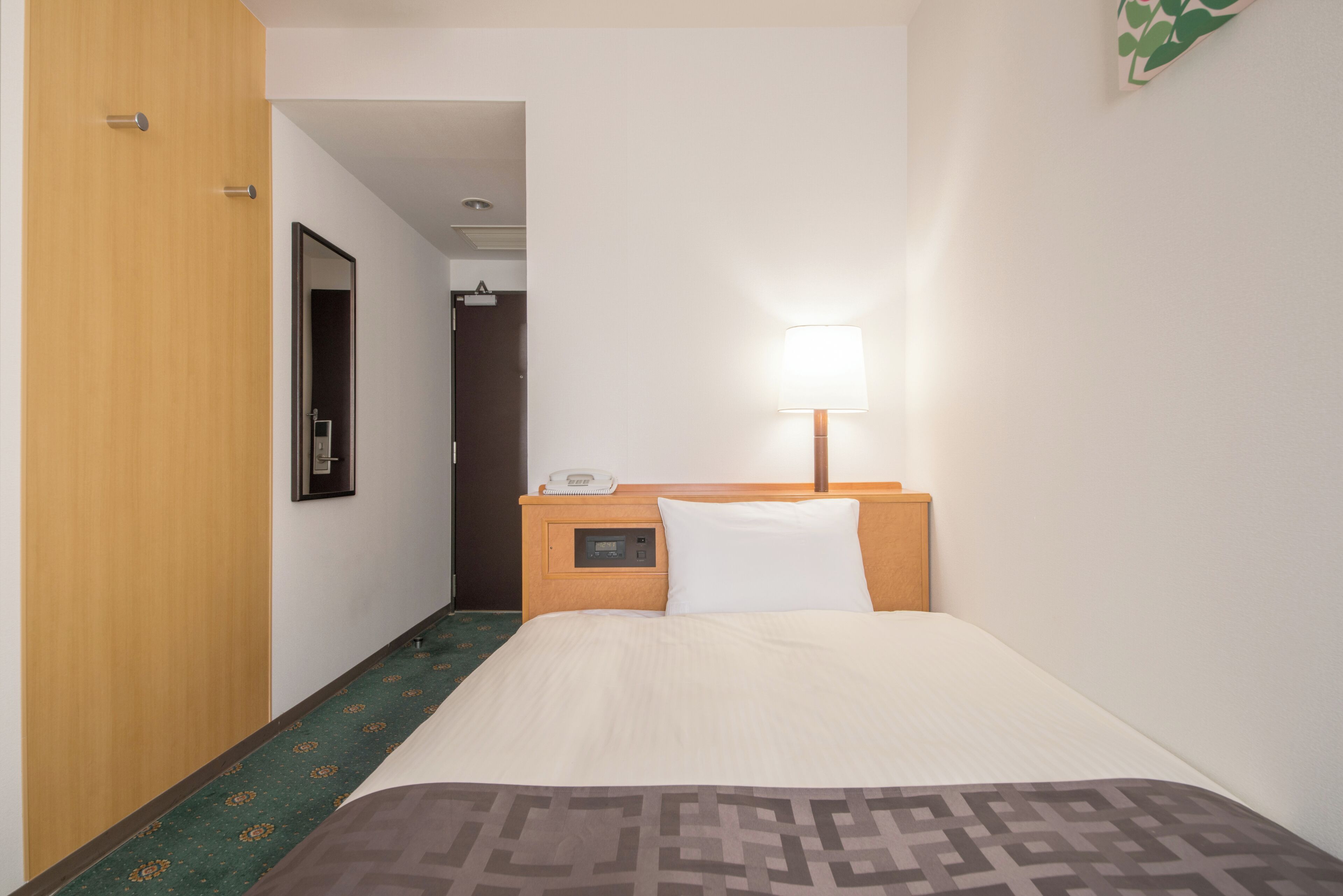 A hotel room with a bed, a bedside table with a lamp, a phone, and a carpeted floor.
