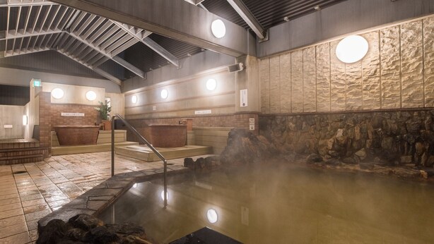 A hot spring area with a stone wall, a wooden bench, and a hot tub. - Premier Hotel Cabin Sapporo (Sapporo)