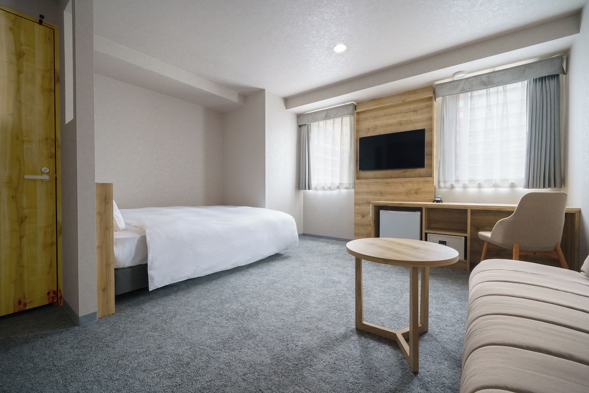 A hotel room with a bed, a desk, a chair, a TV, and a wardrobe.