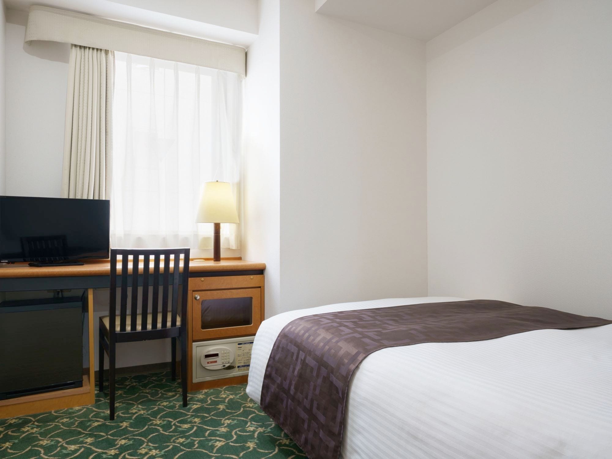 Una habitación de hotel con una cama, un escritorio con una silla, un televisor y una lámpara.
