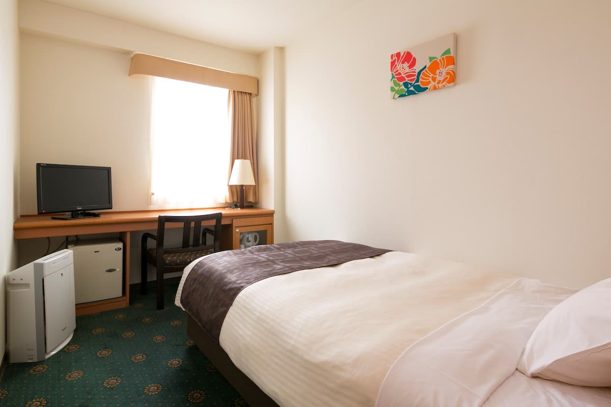 A hotel room with a bed, a desk with a computer, a chair, and a small refrigerator.
