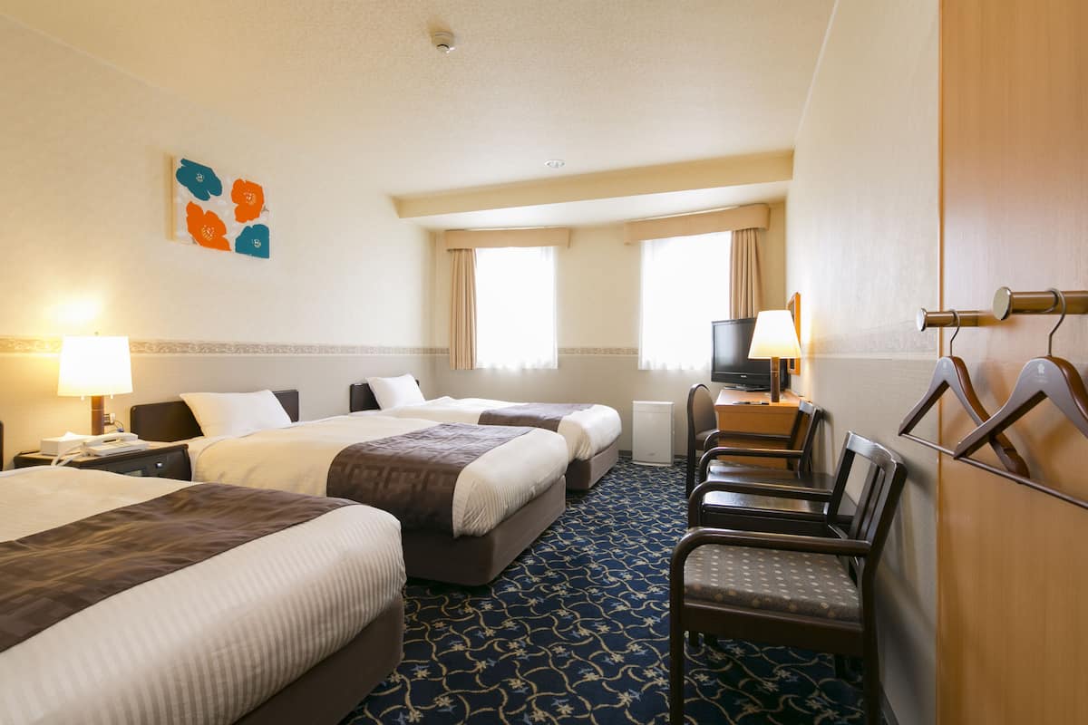 A hotel room with two beds, a desk, a chair, a TV, and a decorative wall piece.