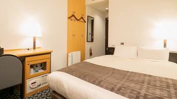 A hotel room with a bed, bedside table, lamp, chair, and a small desk with a telephone.