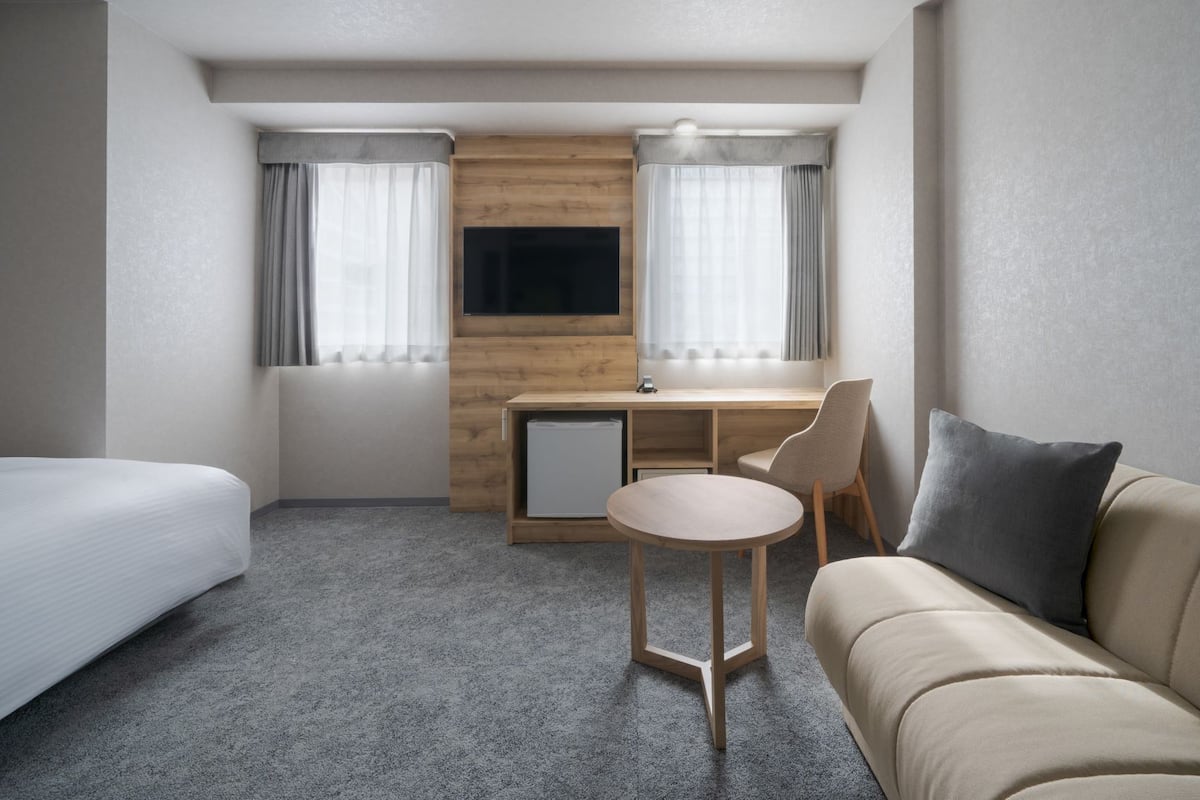 A hotel room with a bed, a sofa, a desk with a chair, a TV, and a small refrigerator.