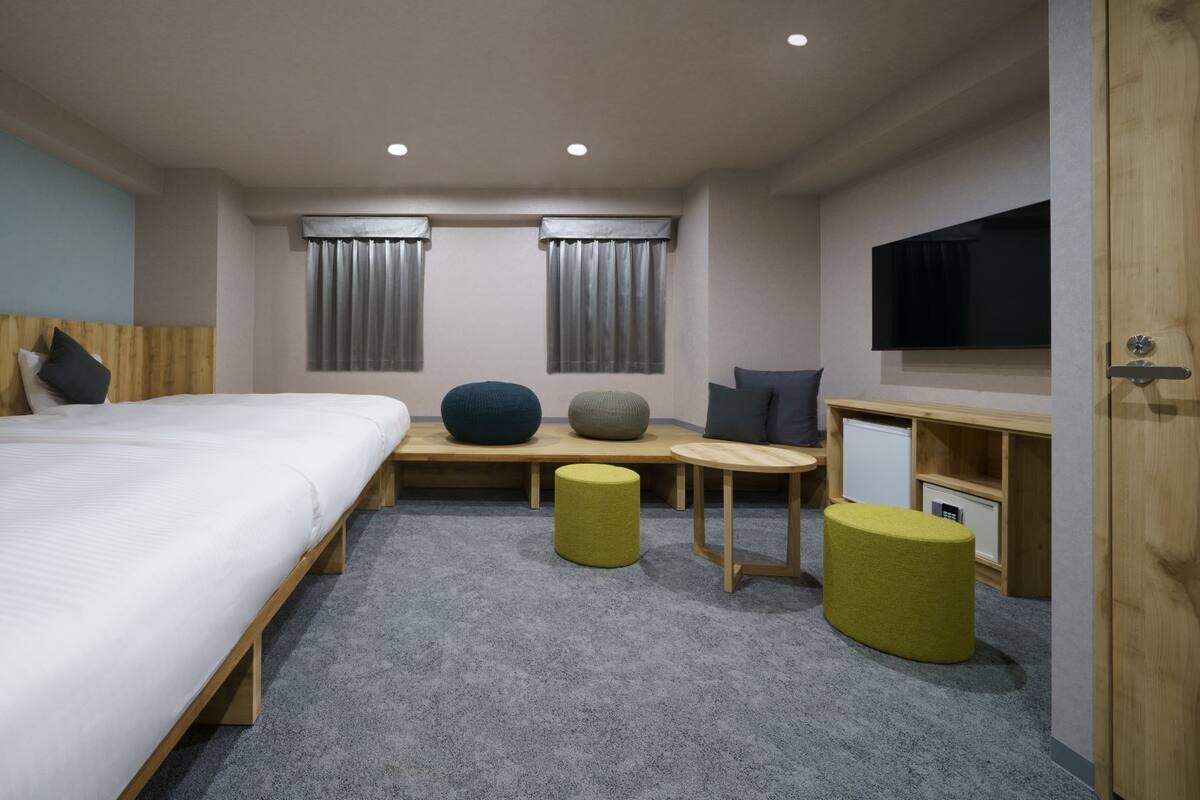 A hotel room with a large bed, a desk, two chairs, a TV, and a small fridge.