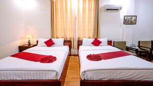 A hotel room with two beds, a nightstand with a lamp, a desk with a chair, and an air conditioning unit on the wall. - Hoang Duc Hotel (Chau Doc)