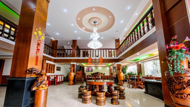 A spacious lobby with a central round table surrounded by stools, a chandelier, and traditional decor. - Hoang Duc Hotel (Chau Doc)