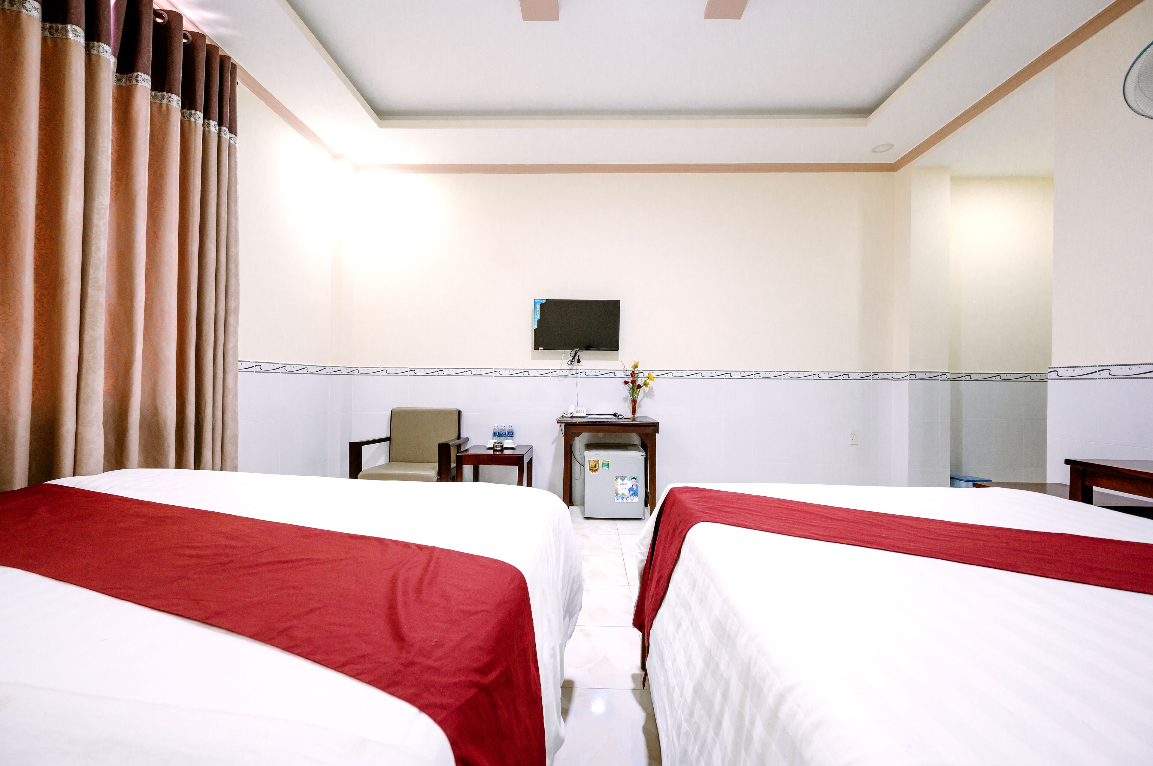 A hotel room with two beds, a television, a desk, and a small refrigerator.