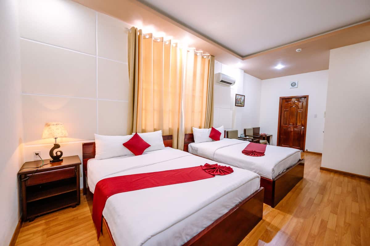 Habitación de hotel con dos camas, suelo de madera, mesita de noche con lámpara y una puerta.