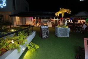 An outdoor seating area with a sign for Sky Pool Bar & Restaurant, surrounded by greenery and palm trees. - Refresh Hotel (Hikkaduwa)
