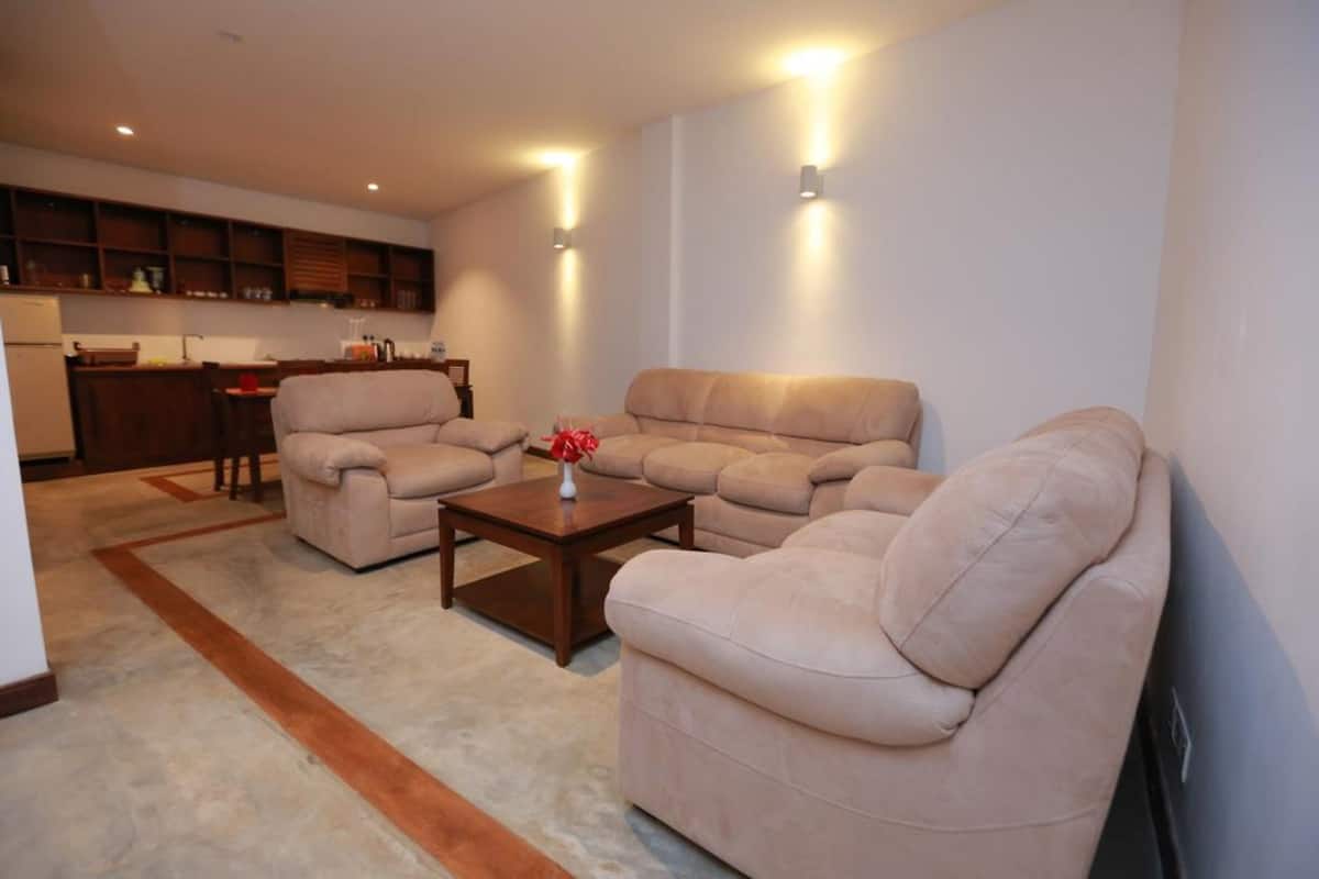 Ein Wohnzimmer mit einem beigefarbenen Sofagarnitur, einem Holztisch und einer Küche im Hintergrund.