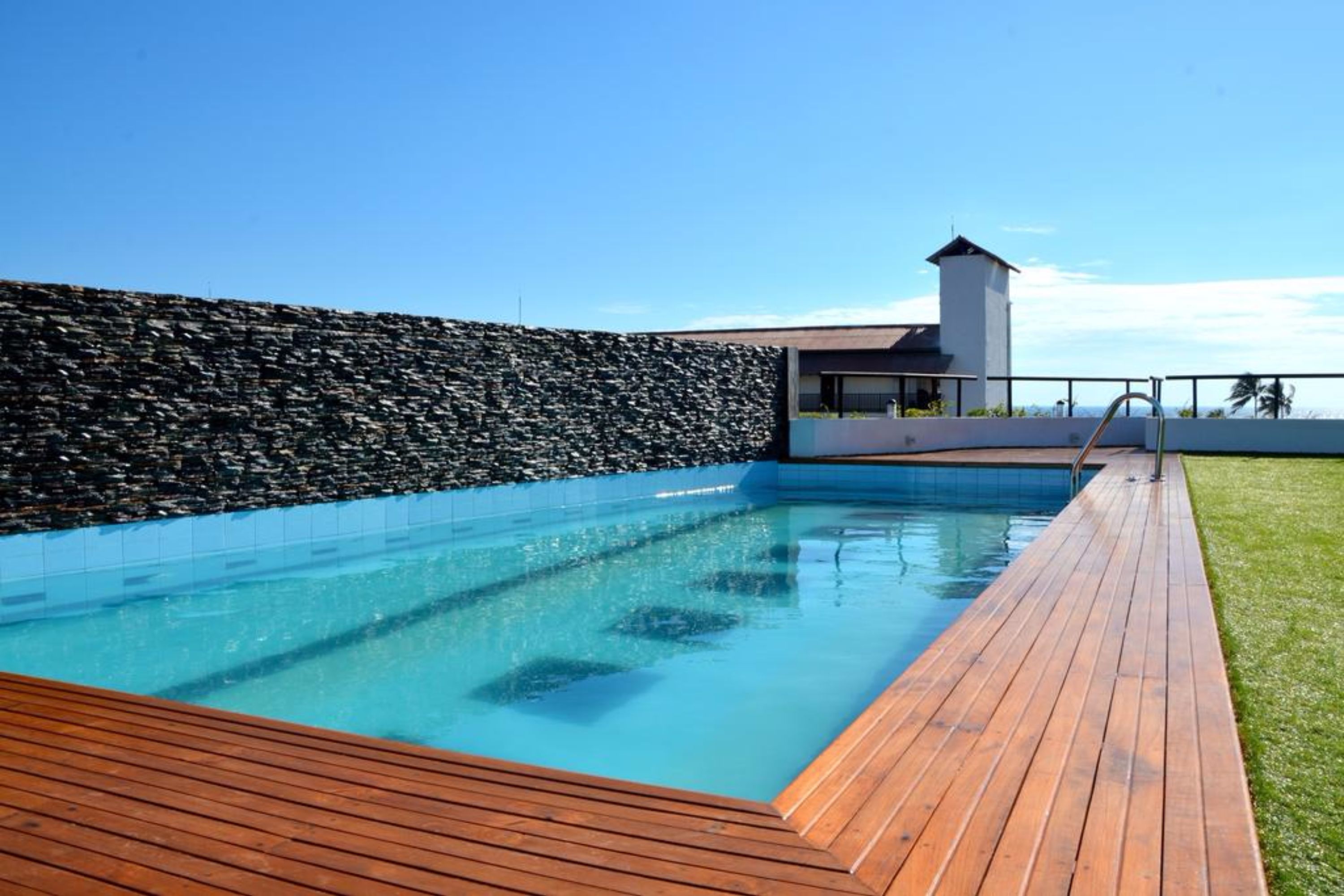 A swimming pool with a wooden deck and a stone wall.