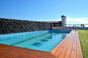 A swimming pool with a wooden deck and a stone wall. - Refresh Hotel (Hikkaduwa)