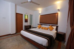 A bedroom with a large bed, a ceiling fan, a nightstand, and a wall-mounted light. - Refresh Hotel (Hikkaduwa)