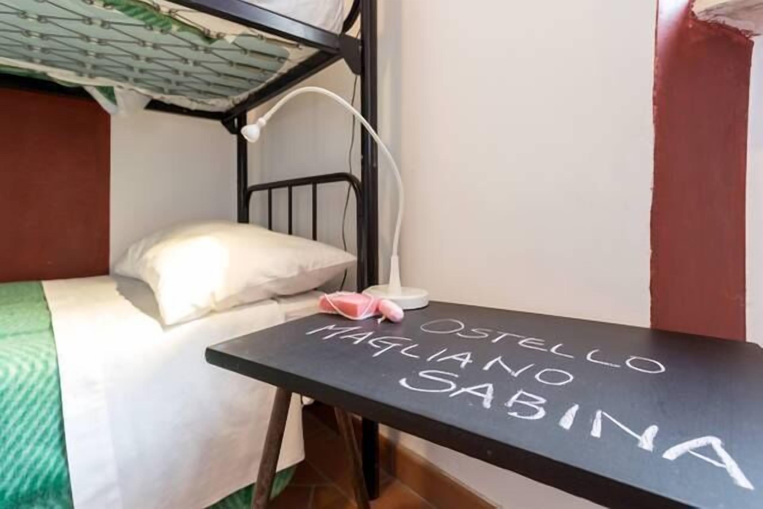 A bunk bed with a white pillow and a black table with the names "OSTELLO MAGLIANO SABINA" written on it.
