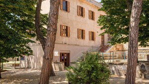 Une cour intérieure avec un bâtiment doté de nombreuses fenêtres et d’une porte, le tout entouré d’arbres et bordé d’un chemin de gravier.