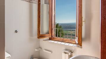 A bathroom with two toilets, a bidet, a sink, and a window with a view of the countryside.