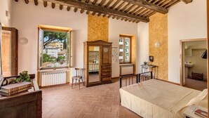 Une chambre à coucher comprenant un lit, une armoire en bois, un radiateur, une fenêtre avec vue et une petite table avec une chaise.