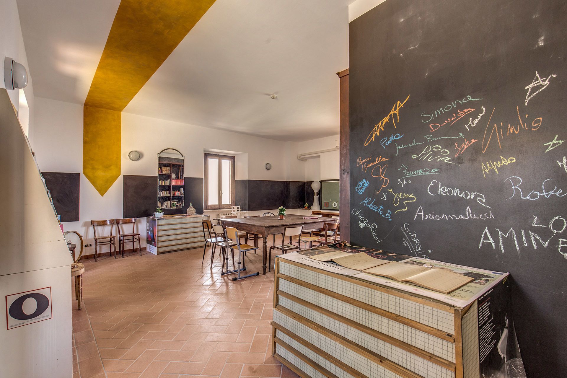 Una biblioteca amplia con una gran pizarra llena de nombres, una mesa de madera y una estantería.