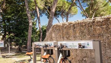 A bike parking area with two bicycles, a stone wall, and trees in the background.