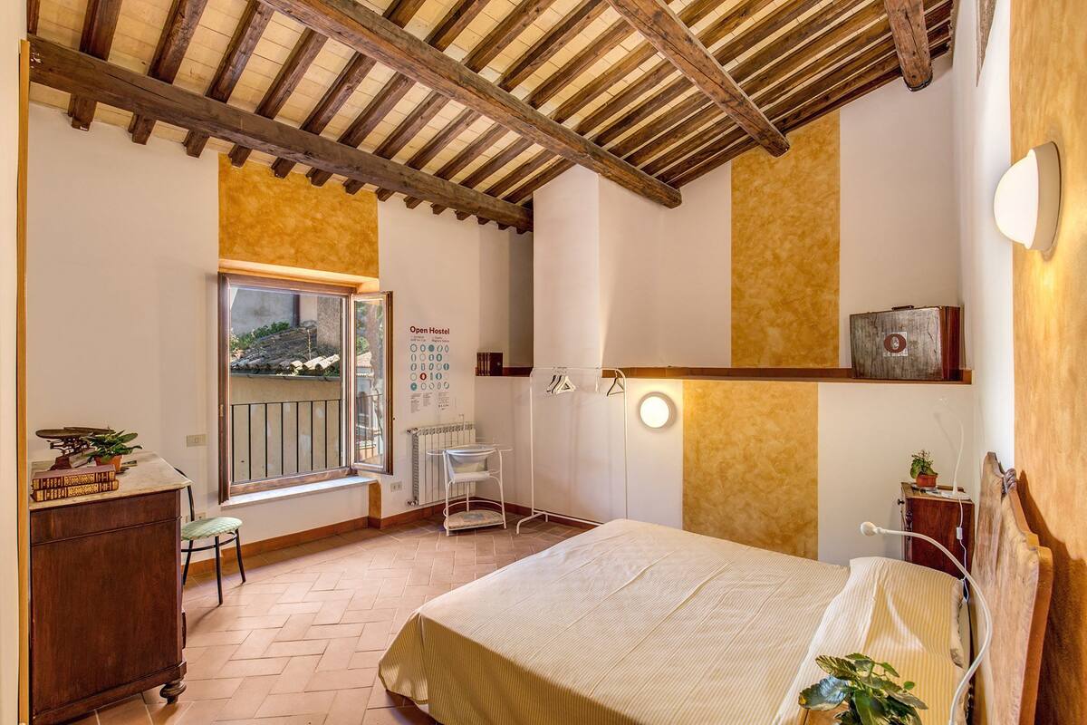 Une chambre à coucher comprenant un lit, un bureau, une chaise, un radiateur, une fenêtre et un luminaire fixé au mur.