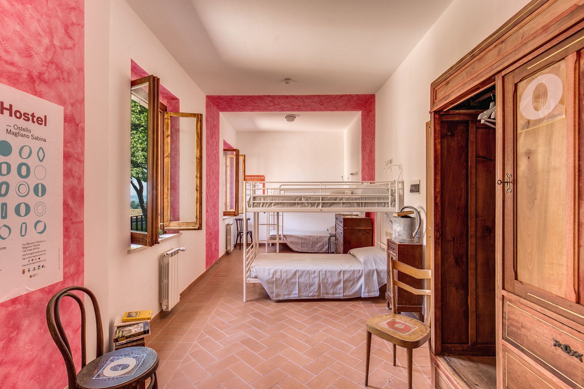Habitación de albergue con una cama individual en literas, un armario de madera, un radiador y un cartel en la pared.